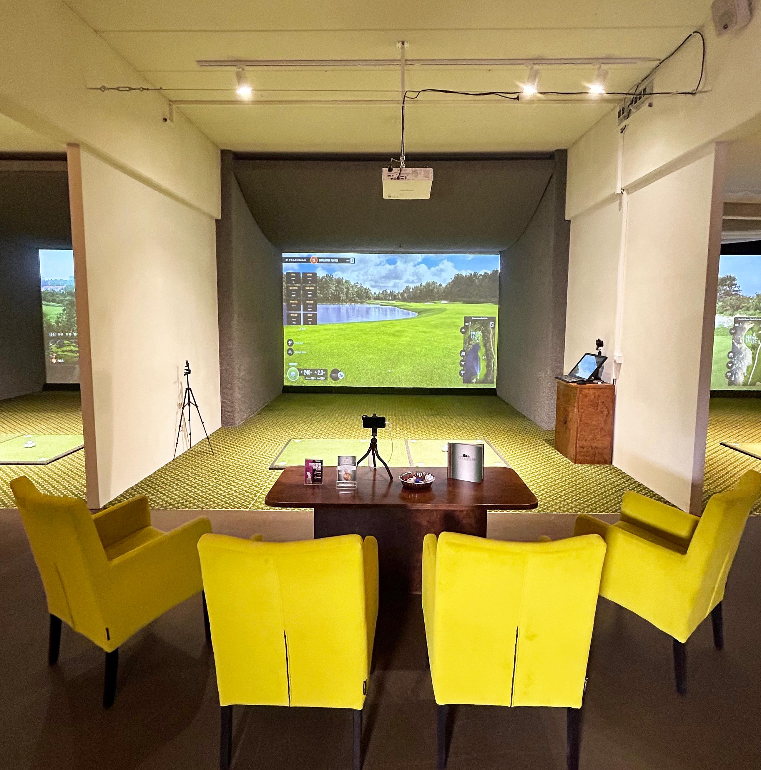 Simulator-Abschlag mit gelben Sesseln, See-Loch auf der Trackman-Leinwand