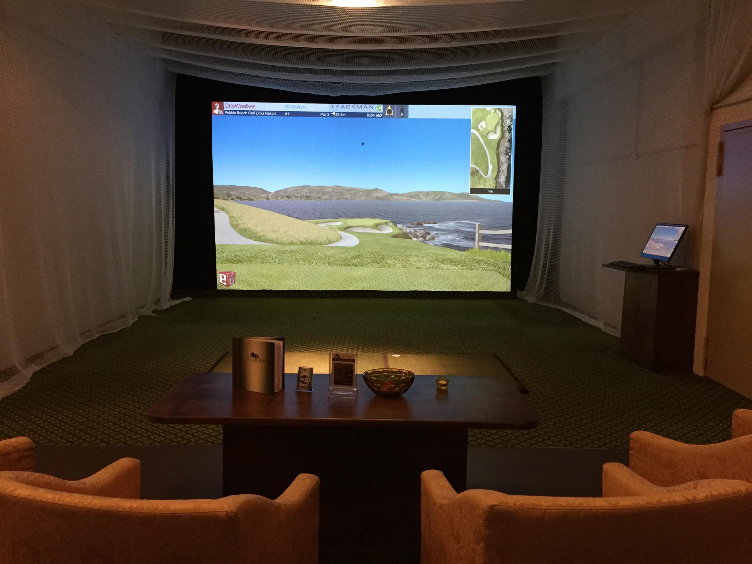 Abschlag mit Pebble-Beach-Loch auf der Leinwand, davor Tisch und gelbe Sessel