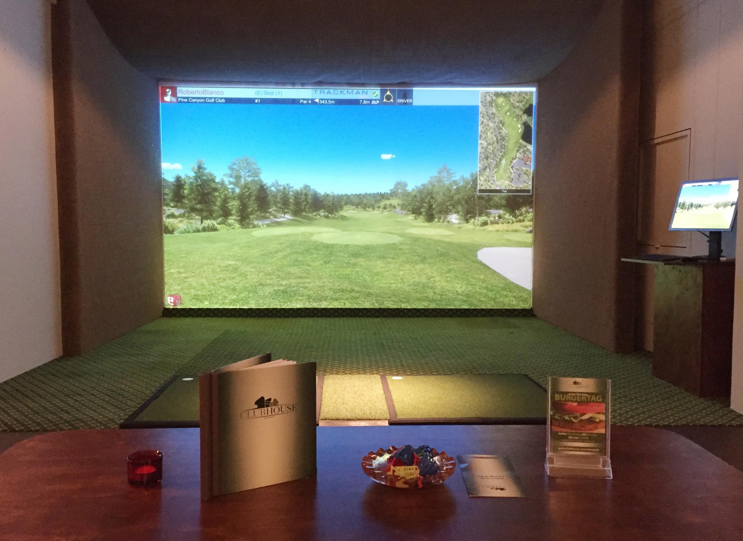 Simulator-Abschlag mit Trackman-Leinwand, davor ein Tisch mit Speisekarte